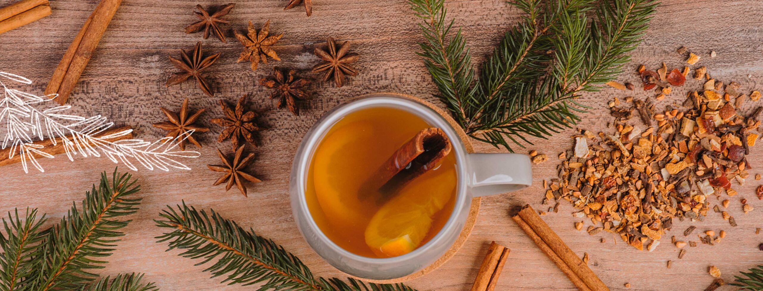 Weihnachtlicher Hintergrund mit Tannenzweigen, Zimtstangen und getrockneten Apfelstücken. In der Mitte befindet sich eine Teetasse gefüllt mit einer winterlichen Teemischung.