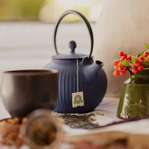Schwarzer Becher, blaue Teekanne, grüne Vase mit Beeren.
